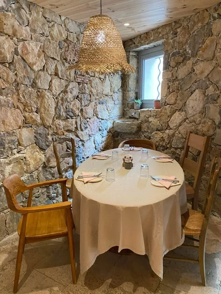Table ronde nappée dans une alcôve aux murs de pierre, sous une suspension en raphia