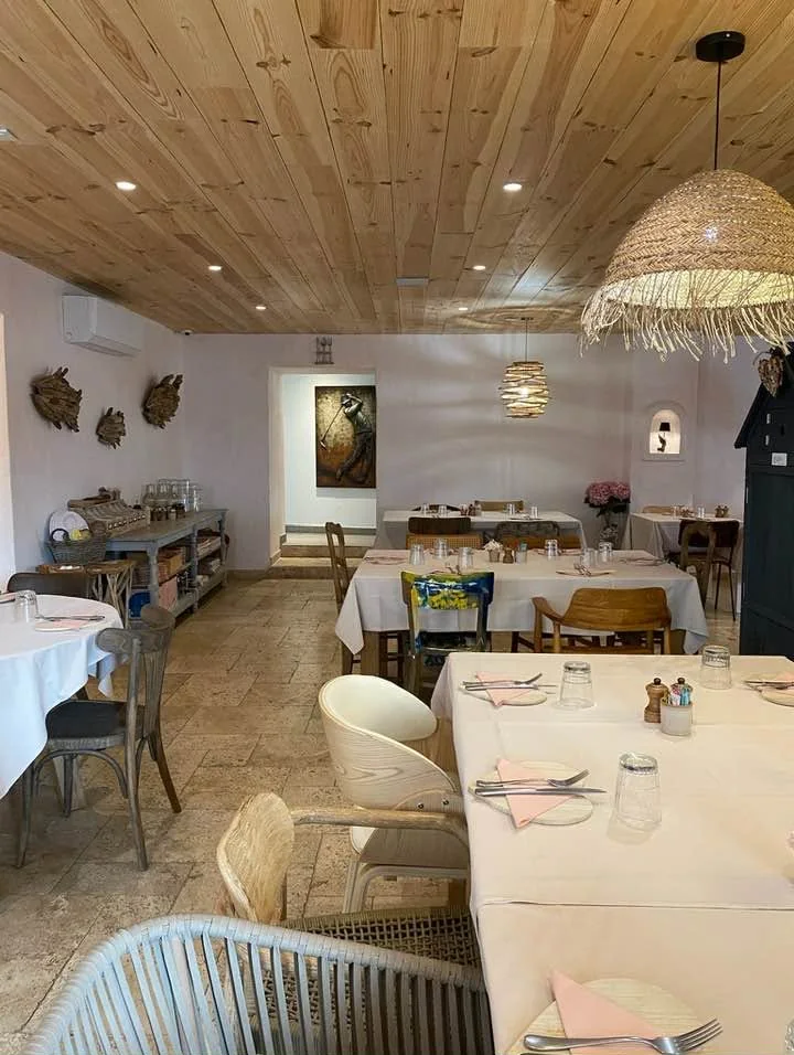 Seconde salle aux murs clairs, tables nappées et fauteuils, plafond de bois