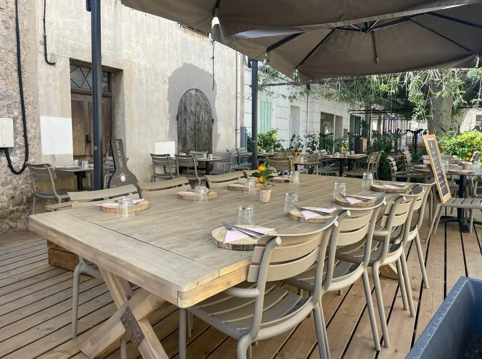 Longues tables en bois dressées sur la terrasse, parasols ouverts